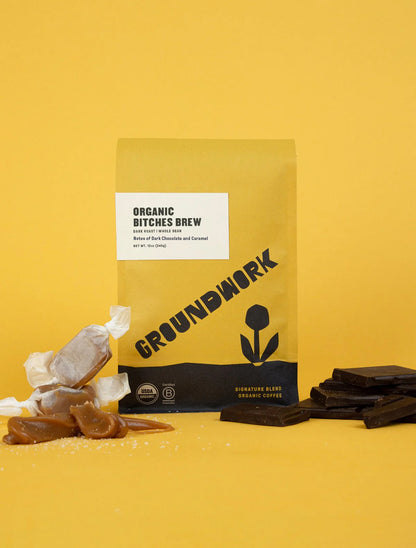 A yellow bag of Groundwork Coffee’s Bitches Brew dark roast is shown with caramel and chocolate pieces on a yellow background.