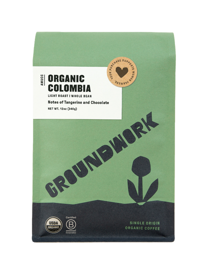 A green and beige bag of Groundwork Coffee’s Colombia: AMUCC Fair Trade whole bean coffee with a flower graphic, certification logos, and notes of tangerine and milk chocolate.
