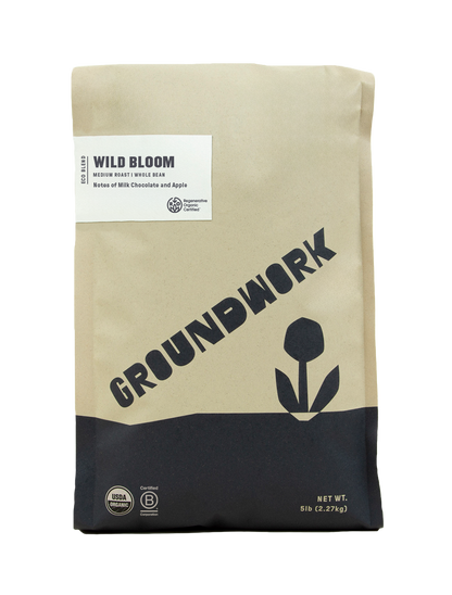 A beige and black 5 lb bag of Groundwork Coffee’s Regenerative Organic Certified® Wild Bloom whole beans with milk chocolate and apple notes, featuring a flower graphic.