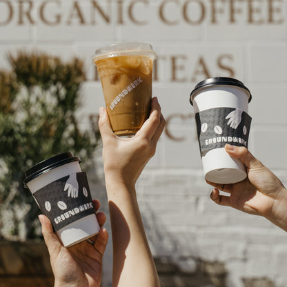 Three hands raise Groundwork Coffee cups at a sunny LA cafe. The In-Store Groundwork Gift Card is the perfect treat for any coffee lover!.