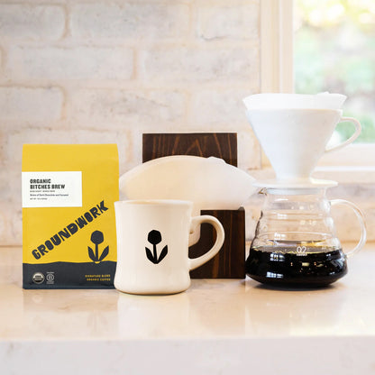 The Hario V60 Pro Kit by Groundwork Coffee includes Organic Bitches Brew, a white mug, filters, and a carafe—perfect for pour-over coffee lovers.