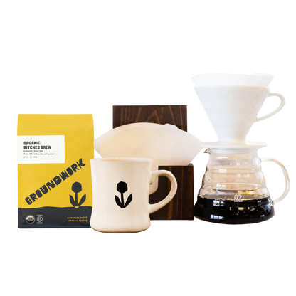 Coffee lovers will love the Hario V60 Pro Kit by Groundwork Coffee, with a yellow bag, mug, dripper, filter holder, and wooden stand on a white background.