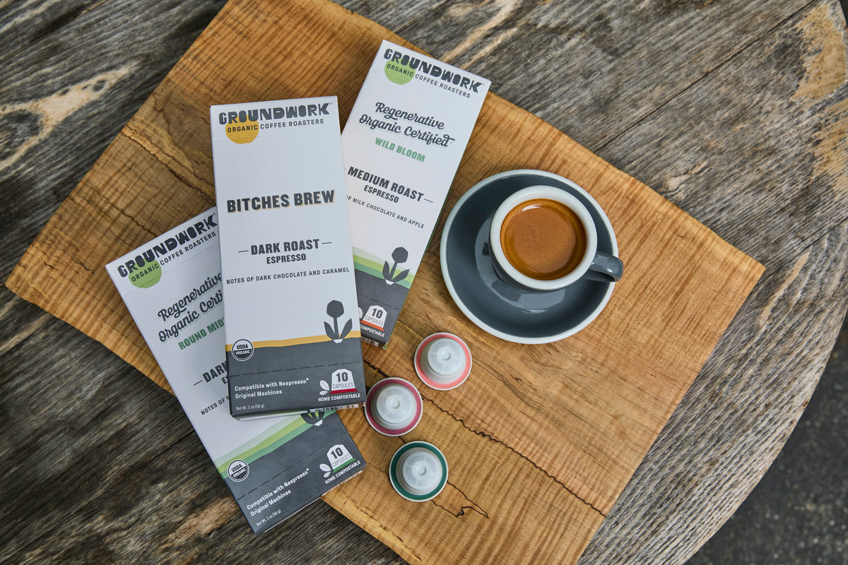 A cup of espresso sits beside the Groundwork Coffee Nespresso® Variety Pack on a wooden surface.