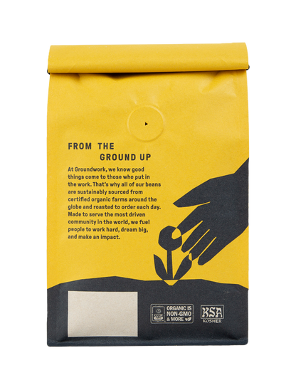 A yellow Big Shot coffee bag by Groundwork Coffee shows black graphics of a hand and sprout, medium roast profile, and organic and kosher logos at the bottom.