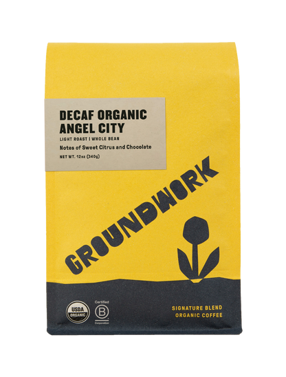 A yellow bag of Groundwork Coffee Decaf Angel City light roast whole bean coffee with sweet citrus notes, tulip graphic, and USDA organic label.