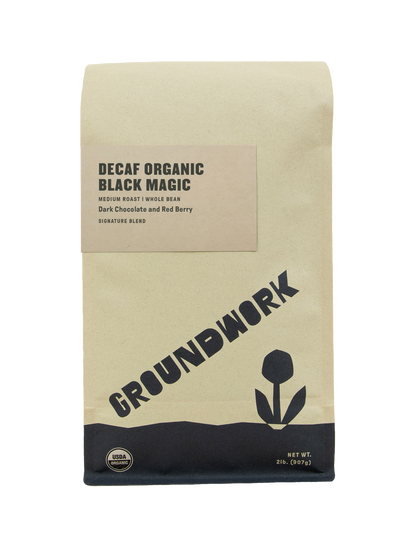 A beige coffee bag labeled Decaf Black Magic Espresso by Groundwork Coffee, with red berry and dark chocolate notes, a flower graphic, and USDA organic seal.