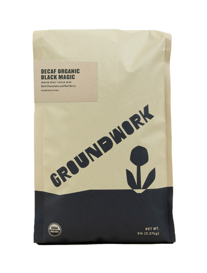 A tan 5 lb bag of Groundwork Decaf Black Magic Espresso, with a black flower graphic, labeled as medium roast, whole bean, with notes of dark chocolate and red berry.