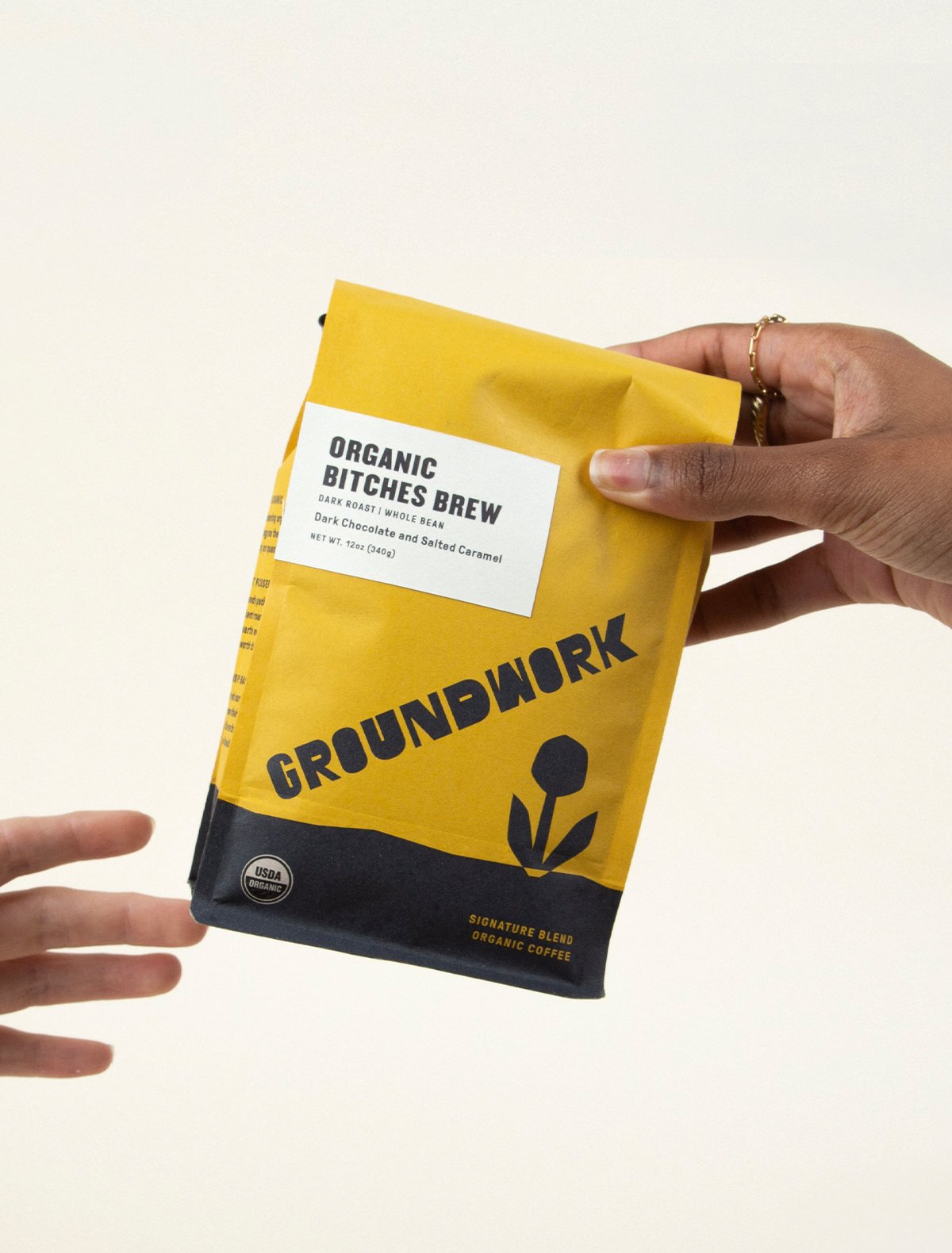 A hand passes a yellow and black bag of Groundwork Coffee Co’s Greatest Gift: Coffee - 3 Months, ideal for gift subscriptions or delivery, against a plain background.