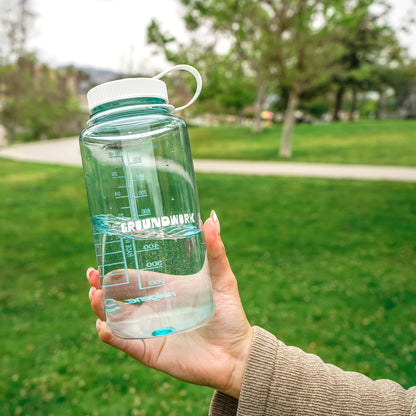 Earth Day 32oz Nalgene with Groundwork logo and white cap girl holding water bottle at the park