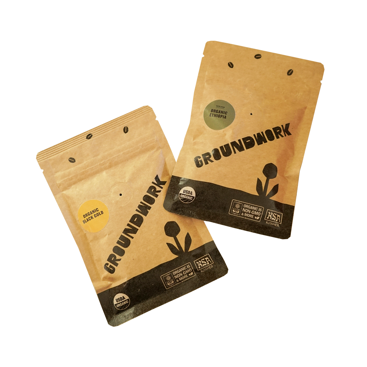 Two small, kraft paper 2oz sample coffee pouches from Groundwork Organic Coffee Roasters displayed on a white background. 
One pouch is labeled “Organic Black Gold” with a small, yellow sticker, and the other is labeled “Organic Ethiopia” with a small, green sticker. 
Both bags feature the Groundwork logo, USDA Organic and KSA Kosher certifications, and a black flower graphic at the bottom.